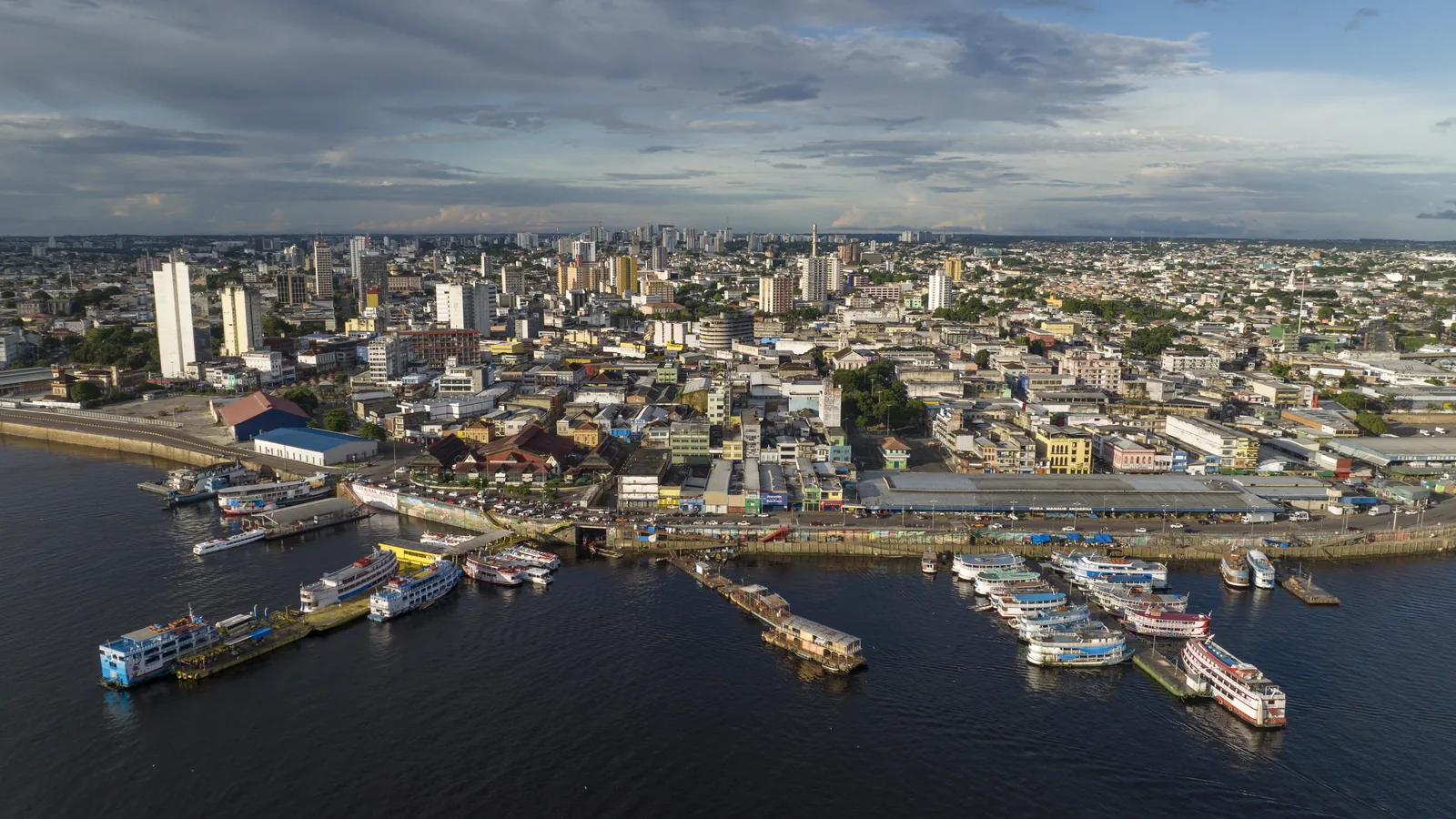 Vista aérea de Manaus, com o porto e os barcos no rio Negro em primeiro plano e os prédios do centro ao fundo